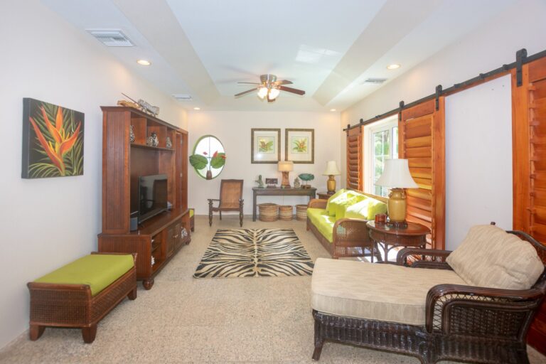 A cozy living room in Roatan, Bay Islands, Honduras, featuring wicker furniture, tropical decor, and bright windows that bring in natural light.