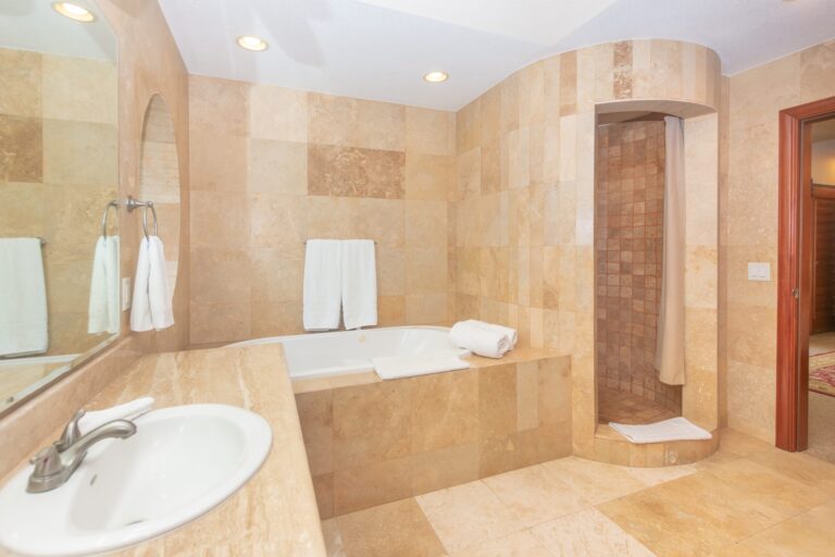 Luxurious bathroom with beige marble tiles, a built-in bathtub, and a walk-in shower with a curtain in Roatan, Honduras.