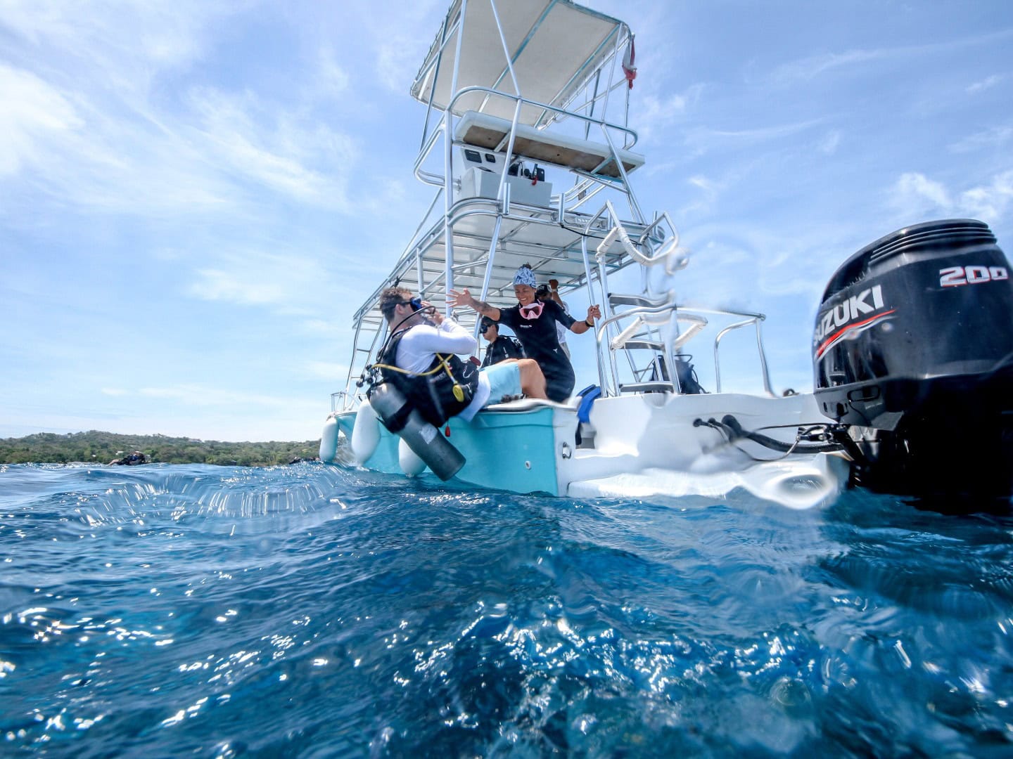 Scuba divers boarding a boat for a diving trip in Roatan, Honduras, with clear blue waters and sunny.