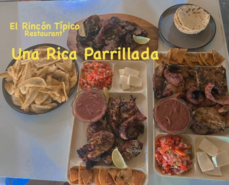 A variety of traditional Honduran dishes, including grilled meats, pickled vegetables, tortilla chips, and salsas, are displayed on plates and bowls at El Rincón Típico restaurant in Roatan, Bay Islands, Honduras.