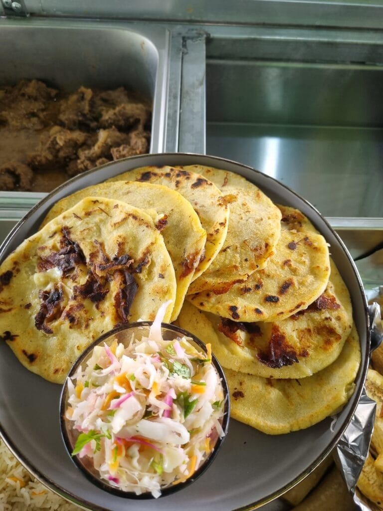 A plate of freshly made tacos with grilled meat, served with a side of colorful coleslaw on a metal tray in a restaurant setting in Roatan, Honduras.
