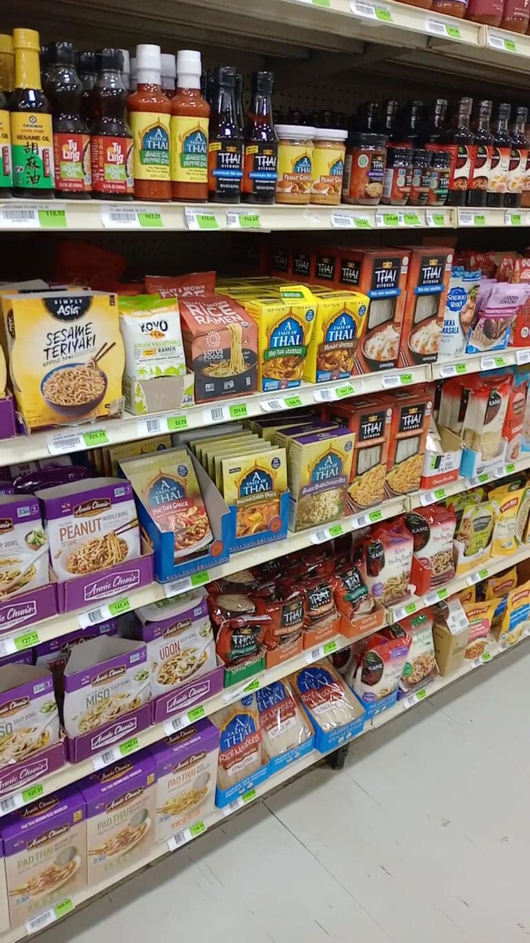 Shelves in a grocery store on Roatan, Honduras display various Asian and Thai food products, including instant noodles, sauces, and ramen packages.
