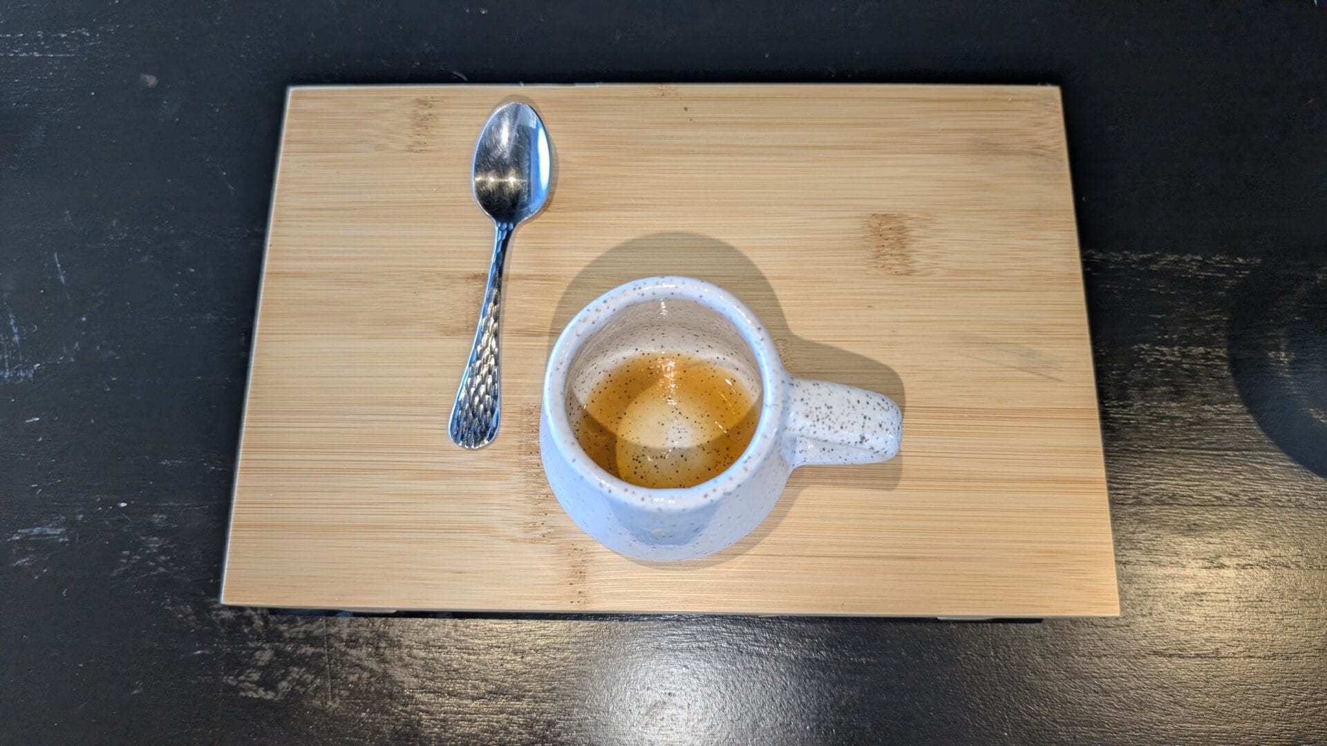A ceramic mug filled with hot tea or coffee, placed on a wooden tray with a metal spoon beside it, on a dark wooden surface in Roatan, Honduras.