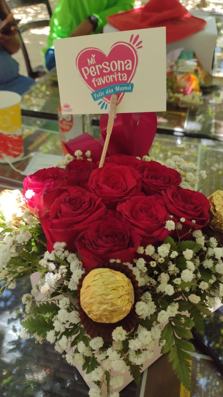 A bouquet of red roses, white baby's breath, and yellow decorative paper lanterns is displayed with a "Feliz día Mamá" card in a floral arrangement on Roatan, Honduras.