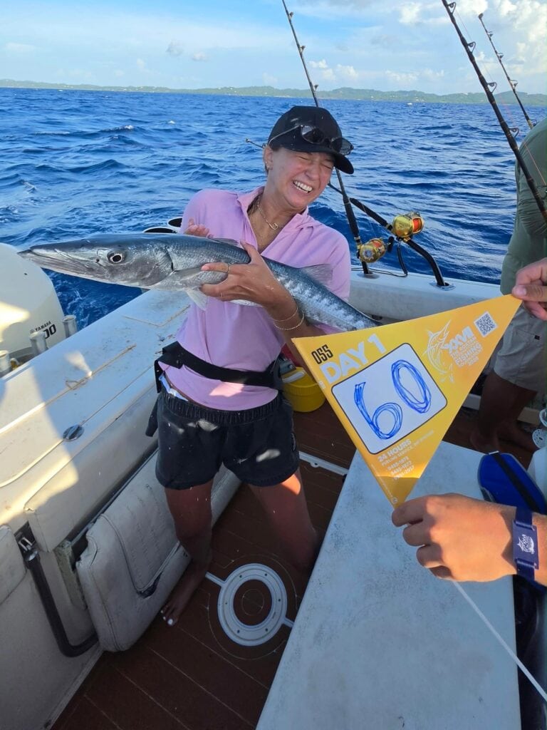A smiling woman holds a barracuda aboard a fishing boat off Roatan, Honduras.