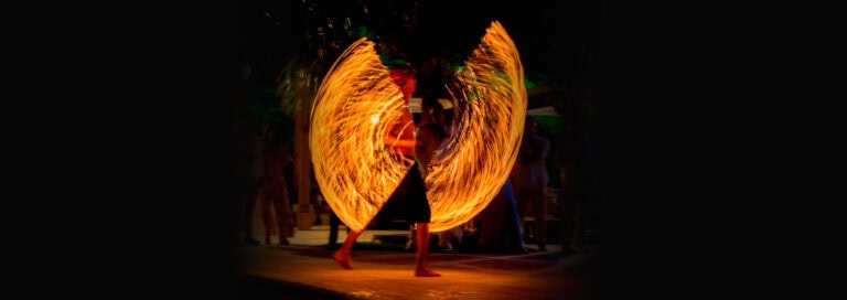 A fire dancer performing at night on Roatan in Honduras, creating swirling patterns with flames surrounded by onlookers.