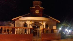 A brightly lit building with a clock tower and a decorative front entrance displaying the word "Welcome" in Roatan, Honduras, at night.