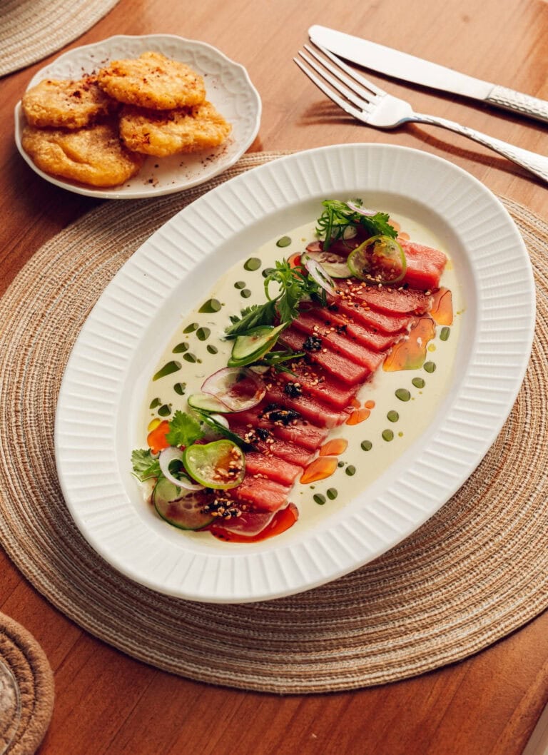 Fresh tuna carpaccio served with microgreens, cherry tomatoes, and balsamic reduction on a white ova.