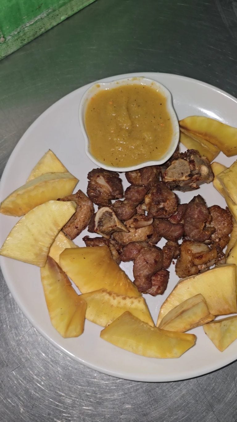 A plate of roasted meat, yellow pineapple wedges, and a small bowl of sauce is displayed on a metal surface in Roatan, Honduras.