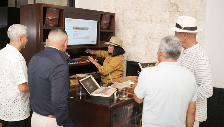 A group of five people gathered around a cigar tasting presentation at a shop in Roatan, Honduras, with a female guide explaining cigar options on the screen behind her.