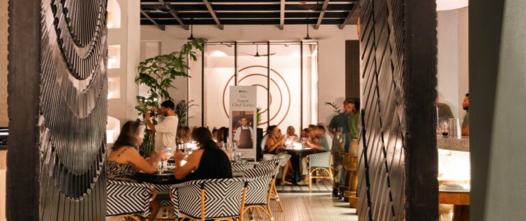 Interior view of a stylish restaurant in Roatan, Honduras, showcasing modern decor, black and white patterned chairs, and guests dining in a warm, inviting atmosphere.