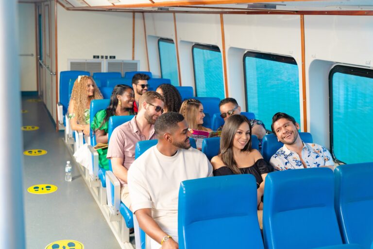 A diverse group of smiling passengers seated in blue chairs inside a boat with large windows, preparing for a trip in Roatan, Honduras.
