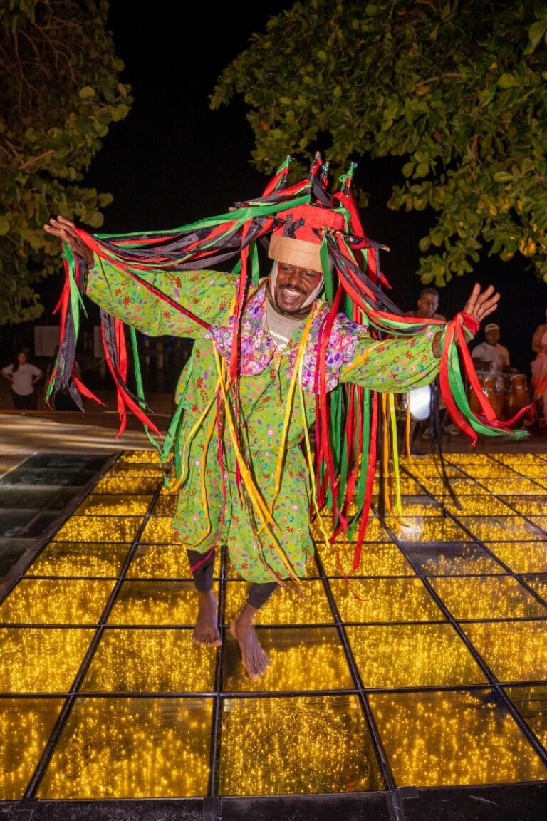 A performer in colorful traditional attire dances on a glowing, illuminated floor during a cultural celebration in Roatan, Honduras.