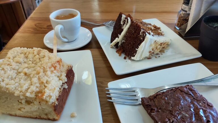 Sweet and savory cakes served on white plates and a cup of coffee displayed on a wooden table in a restaurant setting in Roatan, Honduras.