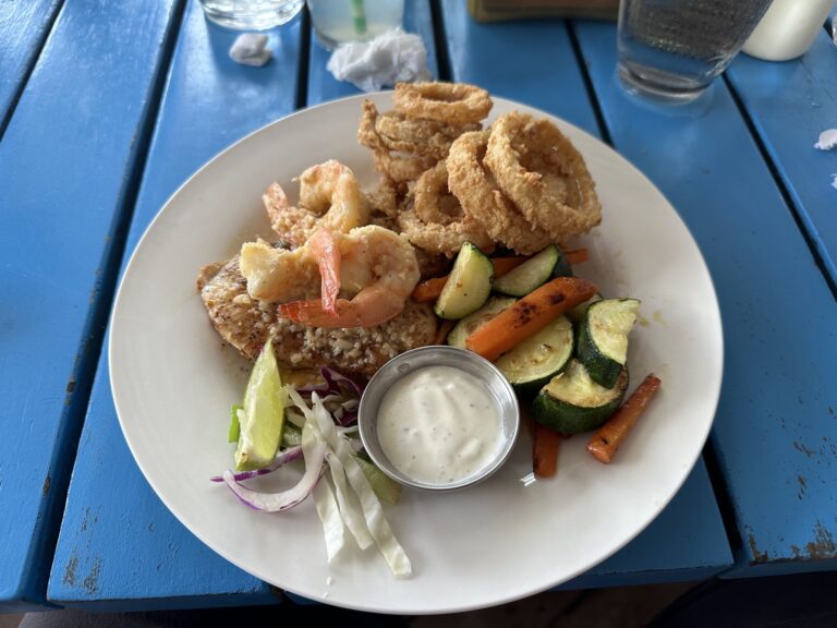 A plate of fried seafood and vegetables with dipping sauce is displayed on a blue table in Roatan, Honduras.