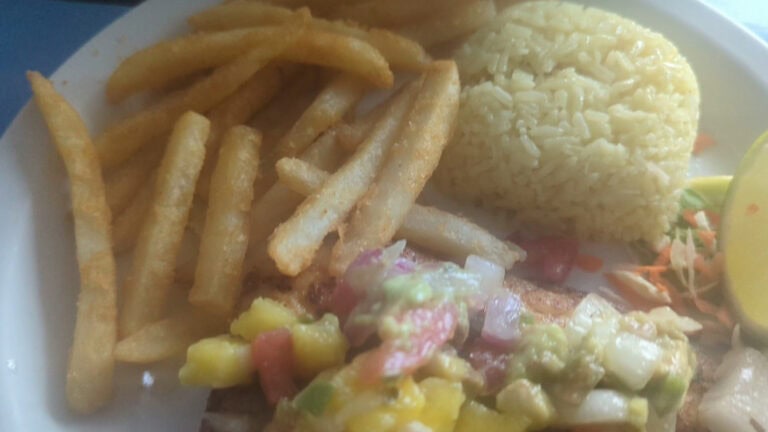 A plate of Costa Rican-style food featuring fried yuca, rice, chopped vegetables, and a small salad, served on a table in Roatan, Honduras.