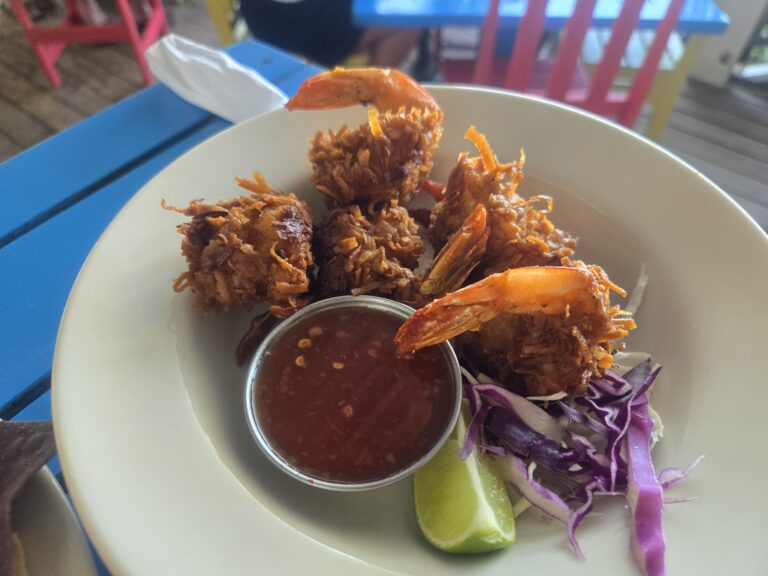 Fried shrimp and coconut rice are served with a side of purple cabbage slaw and lime wedges on a white plate at a restaurant in Roatan, Honduras.