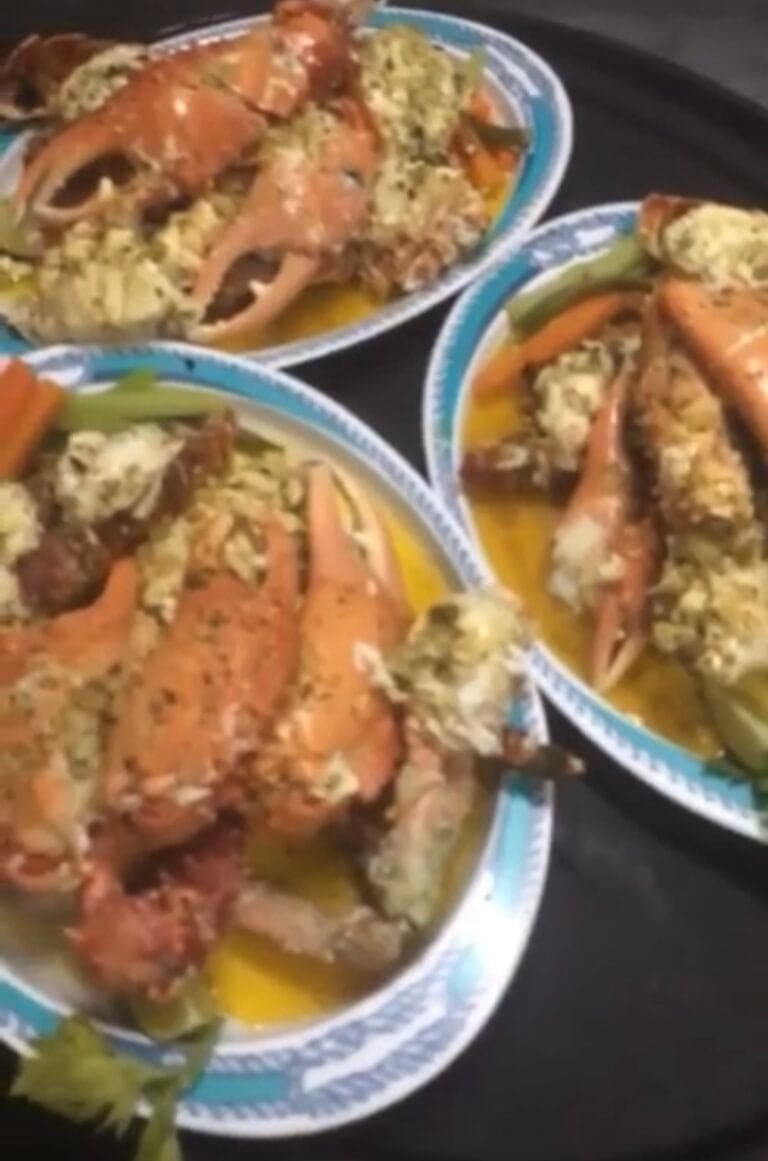 Three plates of Honduran seafood with lobster, rice, vegetables, and herbs are shown on a black table in Roatan, Honduras.