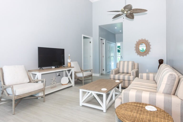 Living room inside a beachfront property on Roatan with white walls, a ceiling fan, and casual striped and neutral-colored furniture.