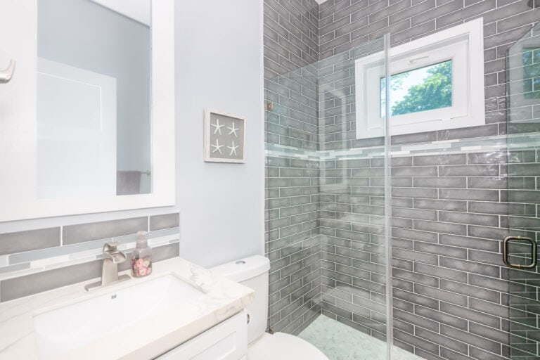 Modern bathroom with gray subway tiles in a house on Roatan, Honduras, featuring a small window with a view of tropical trees.