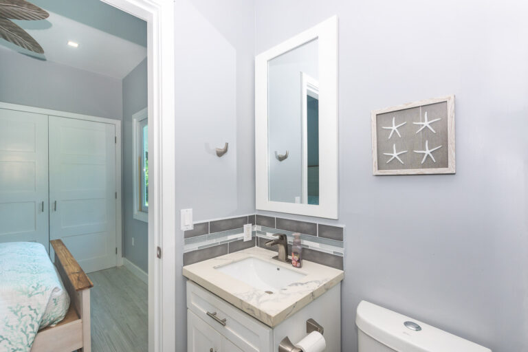 A modern bathroom in a cozy home on Roatan, Honduras, featuring a white vanity with a marble countertop, a rectangular mirror, and starfish wall art with a coastal theme.