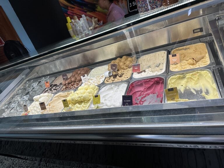 A gelato display case showing various flavors of ice cream with colorful labels, situated inside an ice cream shop on Roatan, Honduras.