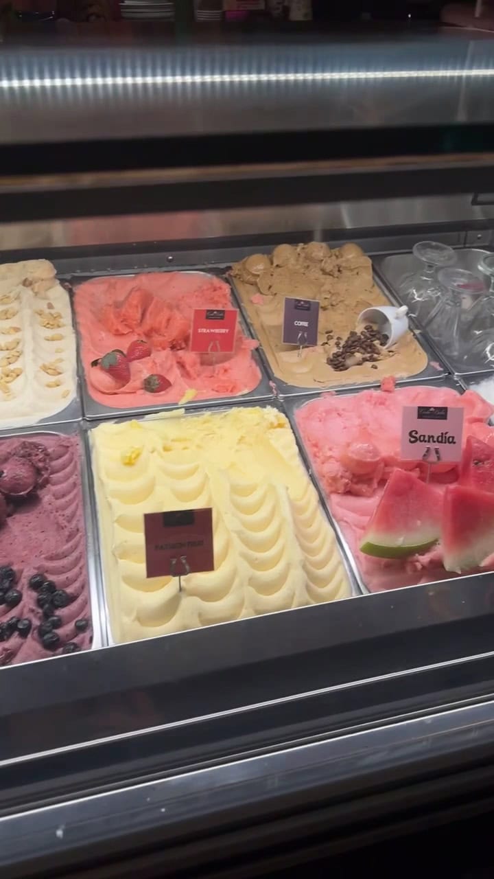 Assorted flavors of gelato with signs indicating different varieties, including strawberry, coffee, watermelon, and others, displayed in a refrigerated case on Roatan, Honduras.