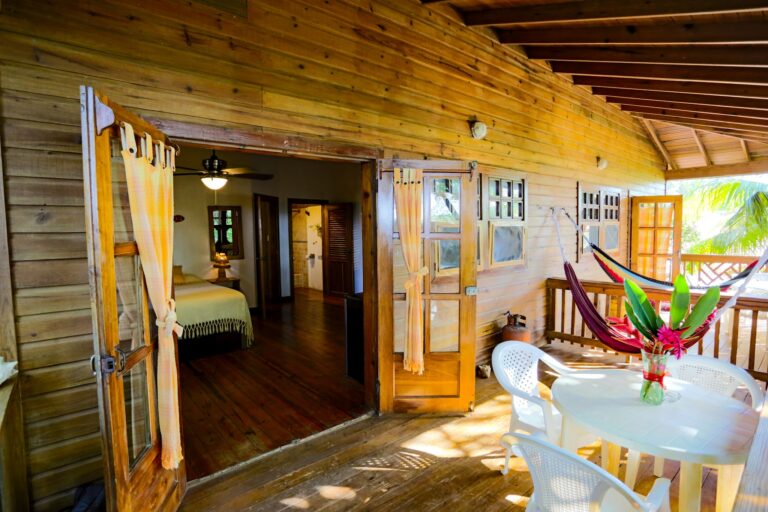 A wooden balcony with sliding glass doors and a hammock showcases a tropical outdoor space in Roatan, Honduras, with lush greenery visible outside.