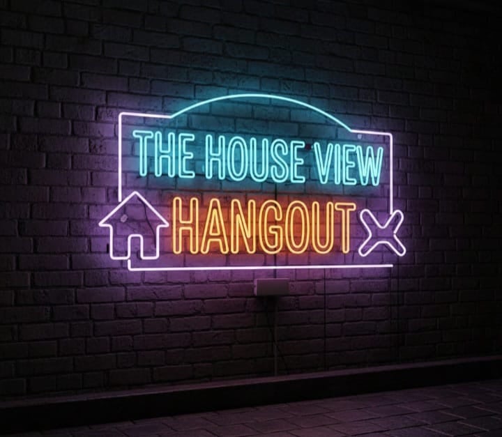 Colorful neon sign on a brick wall displaying 'The House View Hangout' with a house icon and an X symbol, located in Roatan, Honduras.