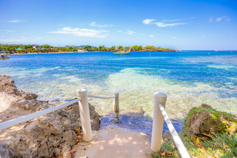Clear blue waters of Roatan, Honduras, with a small stone staircase leading into the sea and lush greenery on the shore in the background.