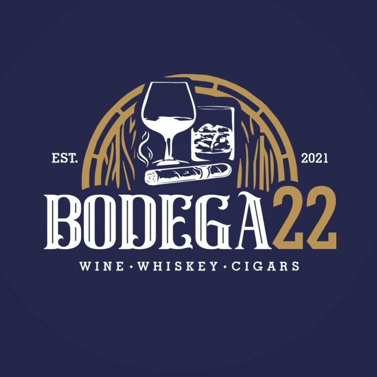 A logo for Bodega 22, a wine, whiskey, and cigar business established in 2021 on Roatan, Honduras, featuring a glass of wine, a glass of whiskey with ice, a cigar, and a background resembling intertwined branches or vines with a navy blue and gold color scheme.