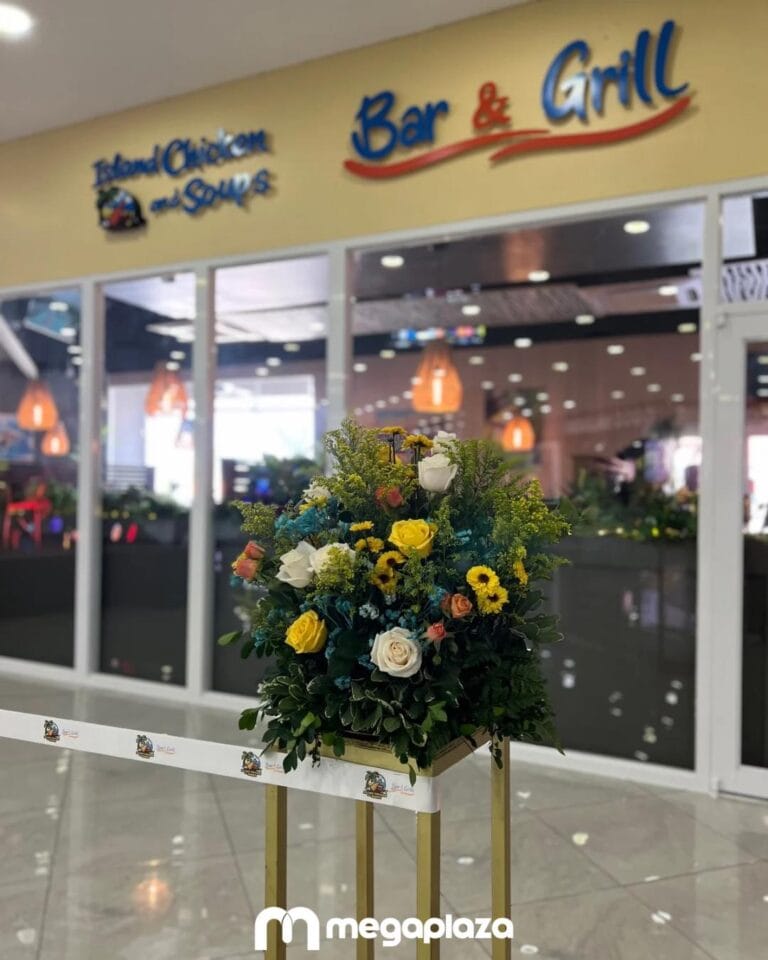 A colorful floral arrangement is displayed in front of a restaurant called Island Chicken and Soups with a Bar & Grill sign, situated inside a shopping mall or commercial area in Roatan, Honduras.