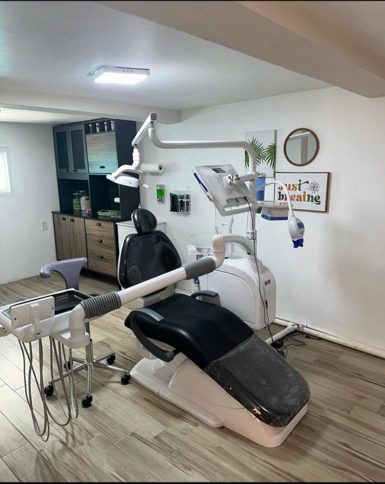 A dental clinic in Roatan, Honduras features a dental chair, overhead lamp, and dental equipment with a decorative wall sign reading "just breathe" and tropical-themed artwork and mirrors on the wall.