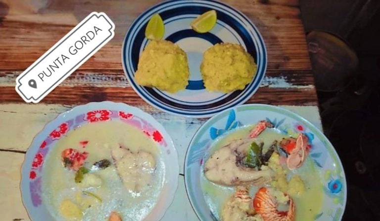 Three plates of traditional Honduran seafood dishes with fish and shrimp served in broth, accompanied by two fried green plantains on a striped plate, displayed on a wooden table in Roatan, Honduras.