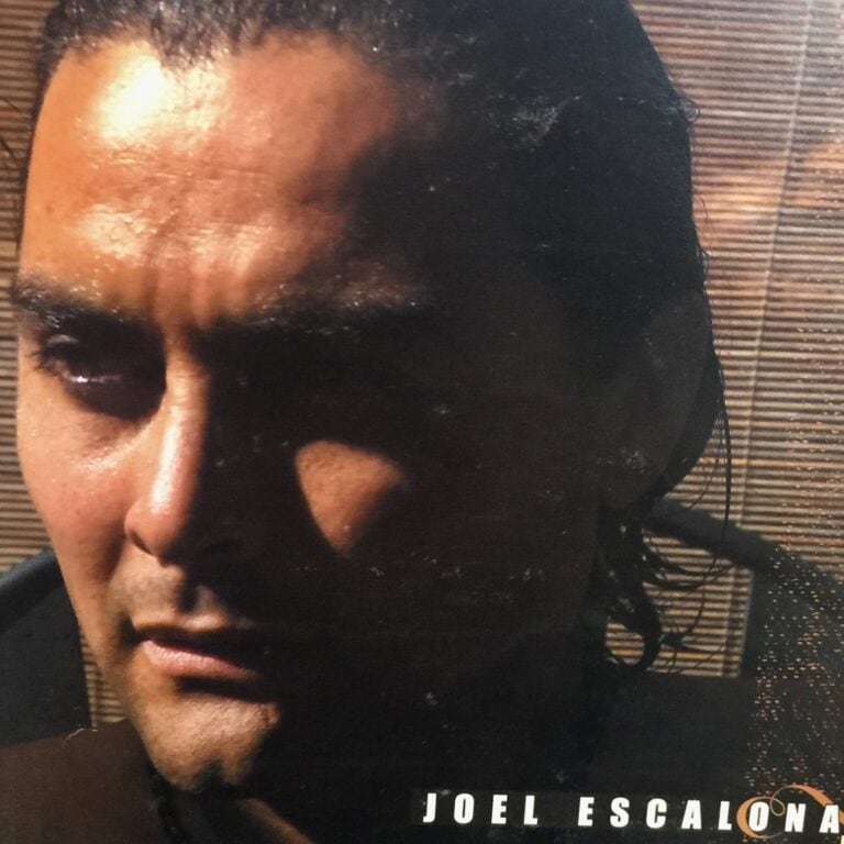 A close-up of Joel Escalona's face with curly hair and facial hair, shown against a background of wooden blinds, on a business listing for Roatan, Honduras.