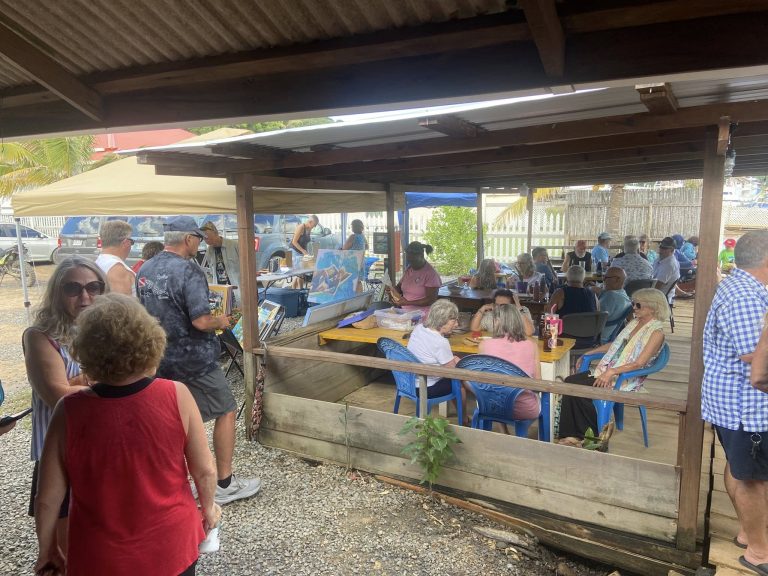 A crowded outdoor dining area with people enjoying food and drinks under a wooden and metal-roofed shelter on Roatan, Honduras.