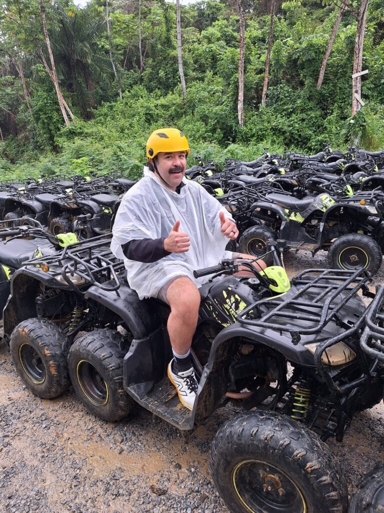 Man riding ATV with helmet, surrounded by multiple ATVs in lush forest.