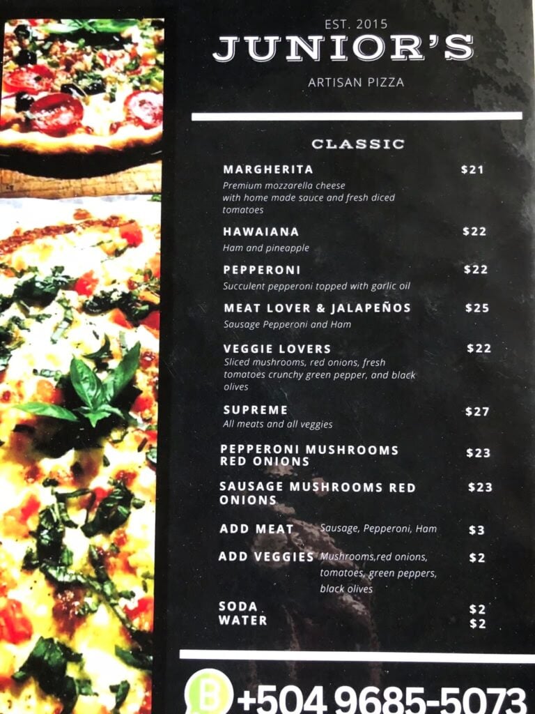 Close-up of a freshly baked pizza with pepperoni, basil, and melted cheese, set against a backdrop of a menu from a Roatan-based pizzeria in Honduras.