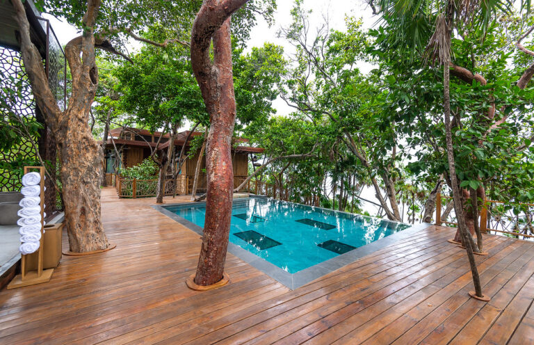 A wooden deck with a modern infinity pool surrounded by lush green trees overlooking the natural landscape in Roatan, Honduras.