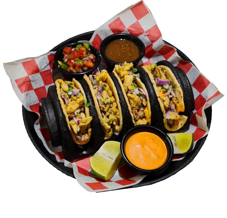 A tray of Baja-style fish tacos served with lime wedges, salsa, and spicy dipping sauces against a white background, representing Roatan and the Bay Islands in Honduras.
