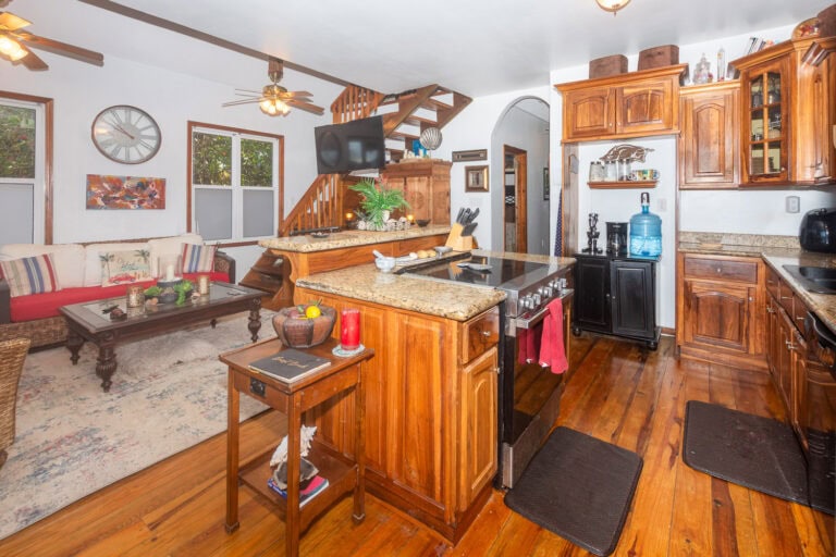 Open-concept kitchen and living room in a cozy Roatan home with wooden cabinetry, granite countertops, and tropical decor elements.