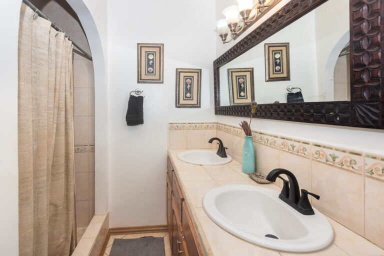 Bathroom featuring a double sink vanity with a large decorative mirror and framed sea life artwork, set in a Caribbean-style home on Roatan, Honduras.