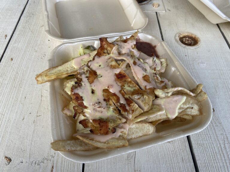 Fish tacos topped with sauce and shredded cabbage are served in a white foam takeout container on a weathered wooden table in Roatan, Honduras.