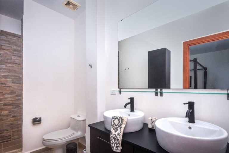 Modern bathroom with two white vessel sinks, black faucets, and a large mirror in a Roatan, Honduras home or business.