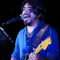 A musician performing with a guitar and singing into a microphone on stage in Roatan, Honduras.