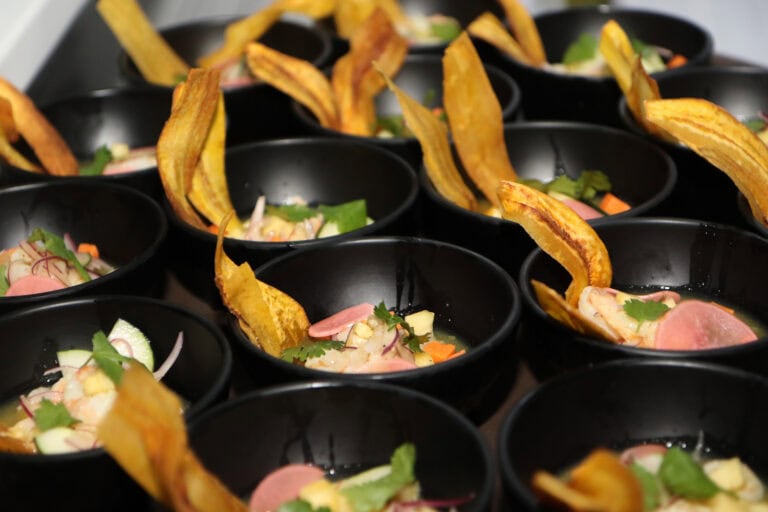 Multiple black bowls of ceviche garnished with plantain chips, vegetables, and herbs arranged on a tray in Roatan, Honduras.