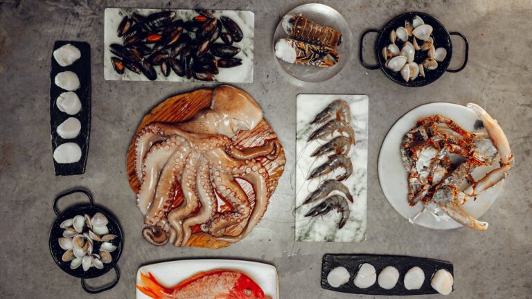Fresh seafood including mussels, octopus, shrimp, lobster, and fish is displayed on plates and trays in a market setting on Roatan, Honduras.