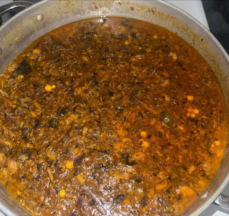 A close-up of a large pot filled with a thick, hearty, dark brown stew containing vegetables and possibly meat, served as a traditional dish in Roatan, Honduras.