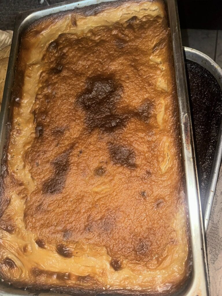 A close-up of a baked dish with a golden-brown crust, likely a casserole or lasagna, displayed in a metal baking pan, typical of cuisine found in Roatan, Honduras.