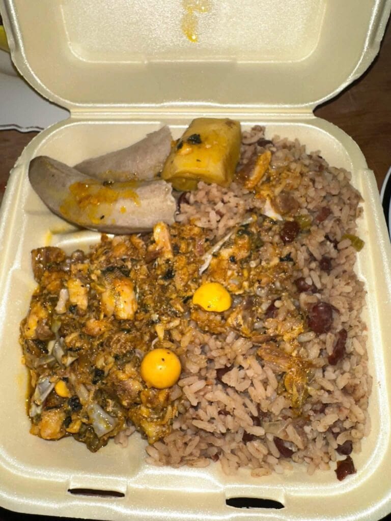 A styrofoam takeout container on Roatan, Honduras, filled with rice and beans, seasoned meat, a tamale, and a banana leaf-wrapped dish.